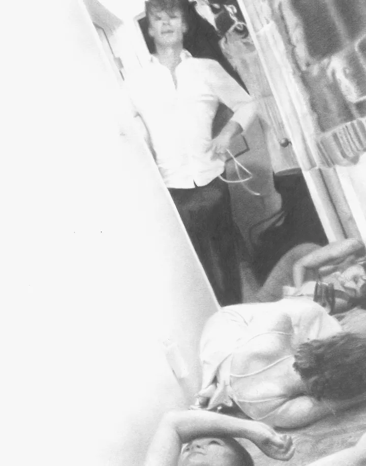 A candid monochrome party scene with a standing figure reflected beyond a reclining guest.